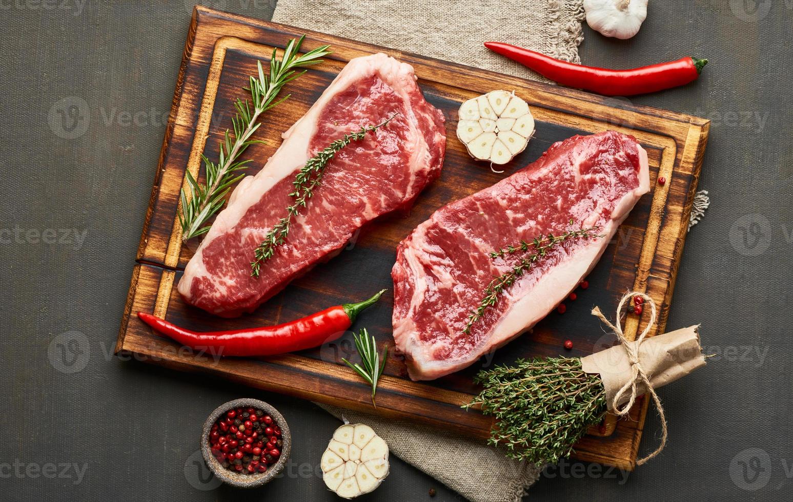 Seasoning raw steak with salt, thyme, garlic. Two big whole piece of raw beef meat photo