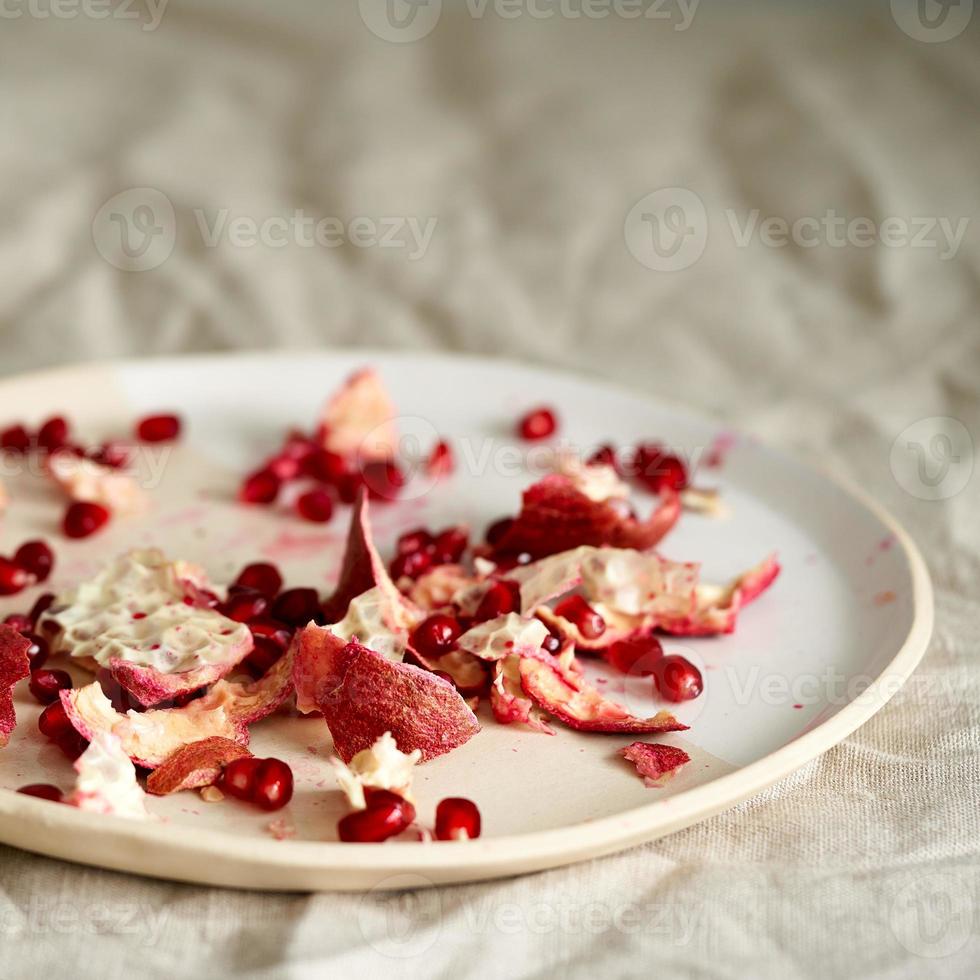 food waste of pomegranate cleaning and seeds on plate on table covered with crumpled beige tablecloth photo