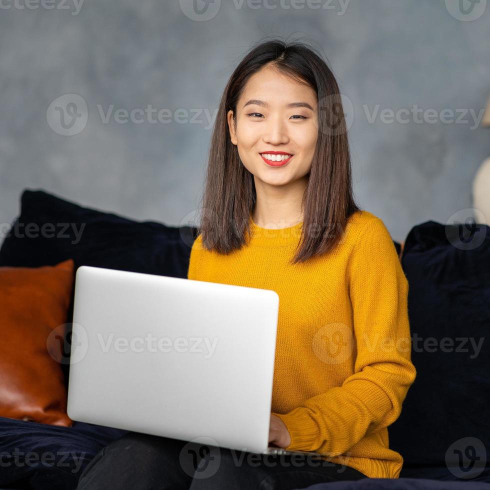 mujer de negocios asiática que trabaja en la computadora portátil en el sofá. empresaria japonesa trabaja en casa foto