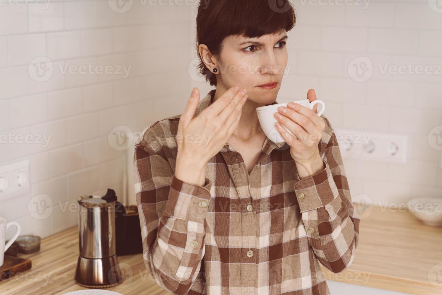 COVID-19 causes loss of smell. Woman sniffing smell of coffee from cup while preparing drink photo