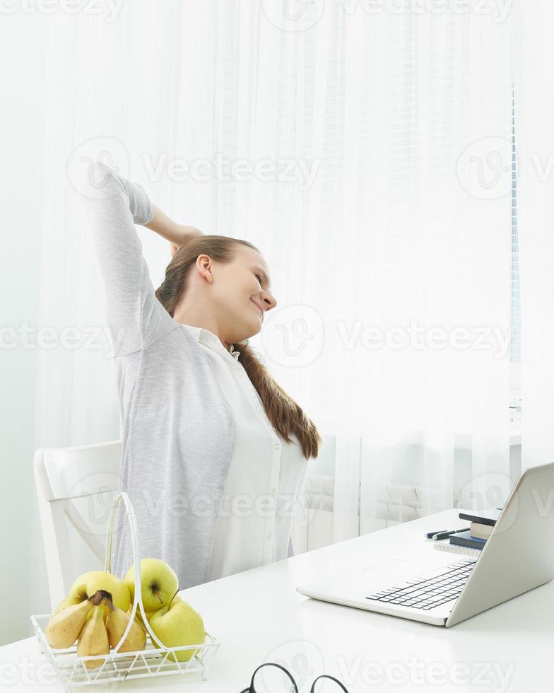 Woman stretches her arms, kneads her back from fatigue. Long sitting at computer, muscle cramps. photo