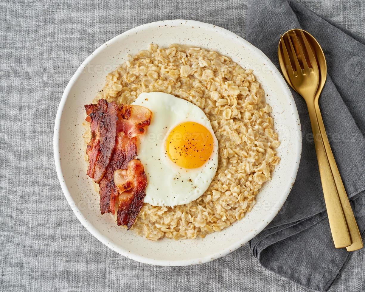 Oatmeal, fried egg and fried bacon. Hearty fat high-calorie breakfast, source of energy. photo