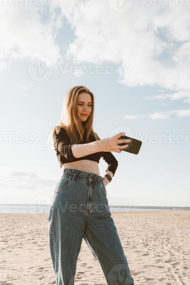 Low angle of beautiful woman taking selfie on ocean or sea coastline. photo