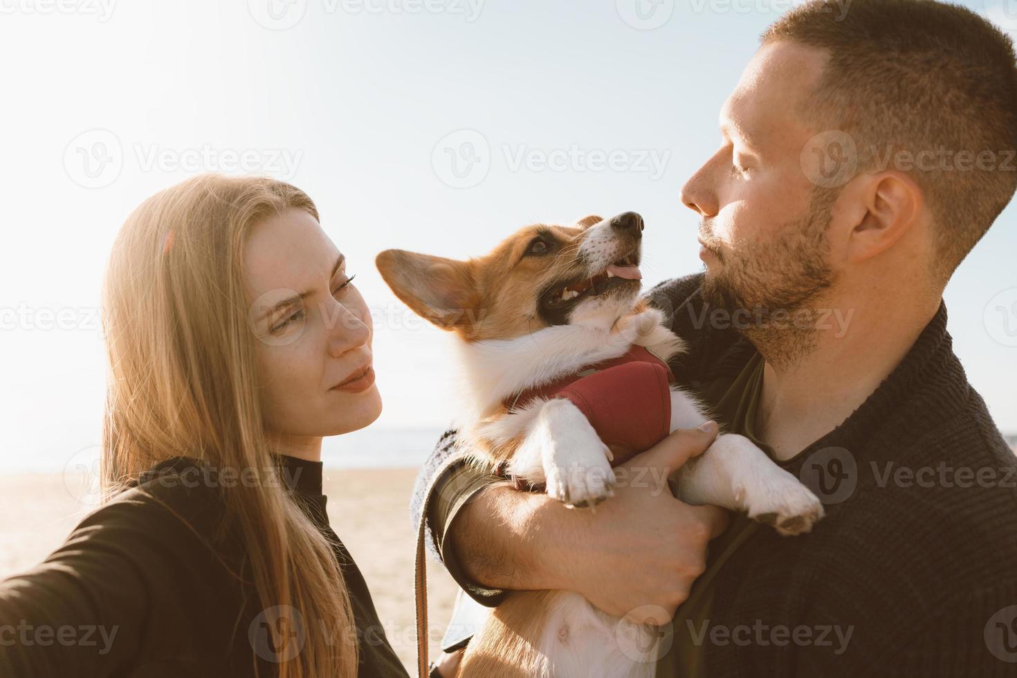 joven familia feliz con perro disparando en la playa. hermosa chica y chico y corgi foto