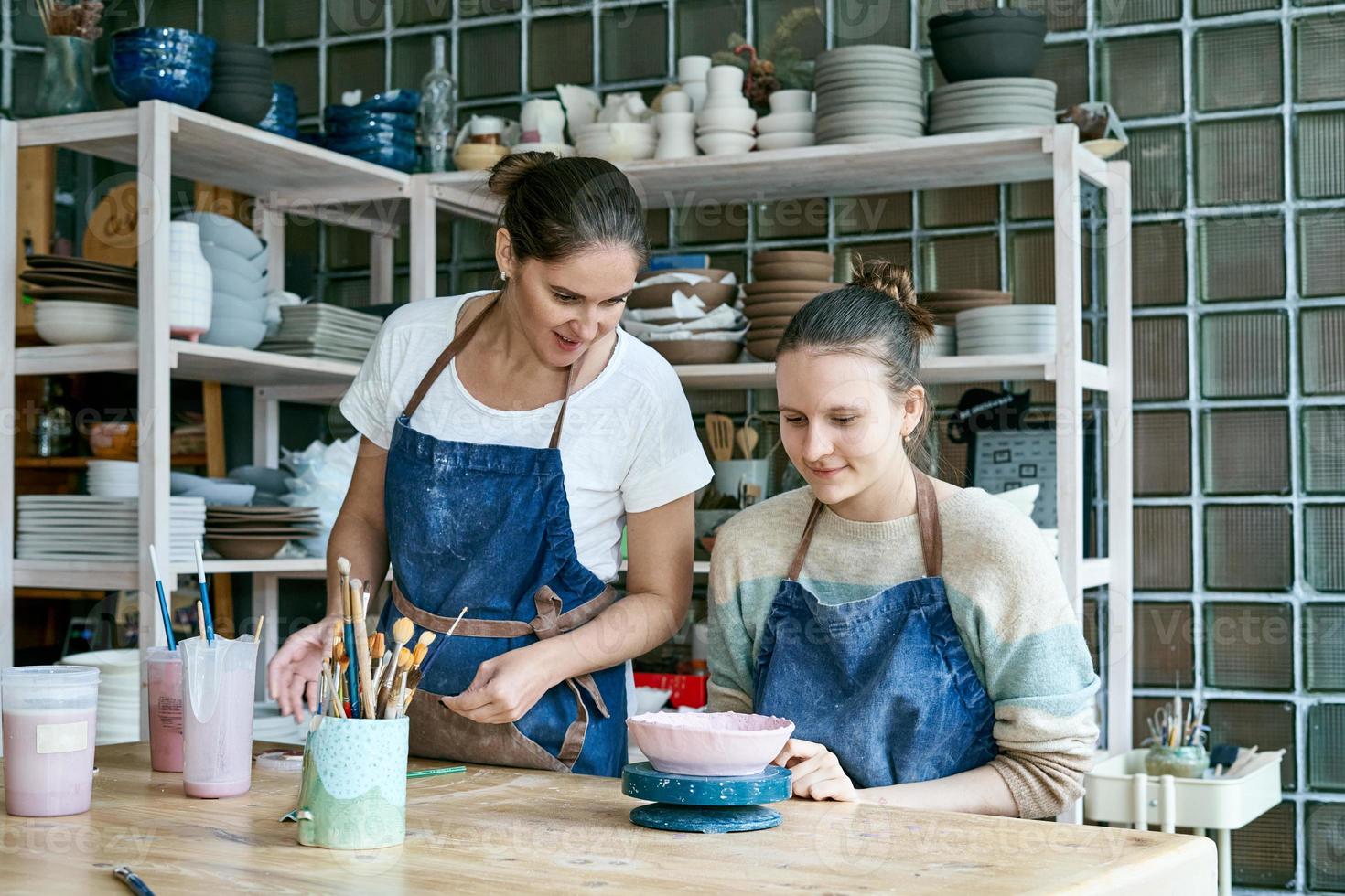 mujer haciendo cerámica. atractiva joven calificada en delantal de pie en la mesa y enseñando foto