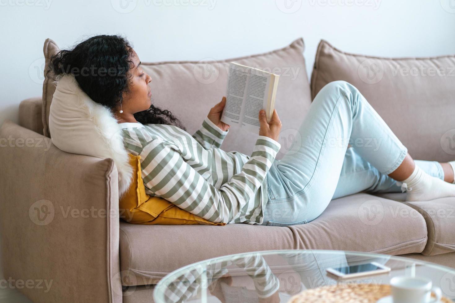 African-american female having rest on sofa and reading book. Being offline for digital detox photo