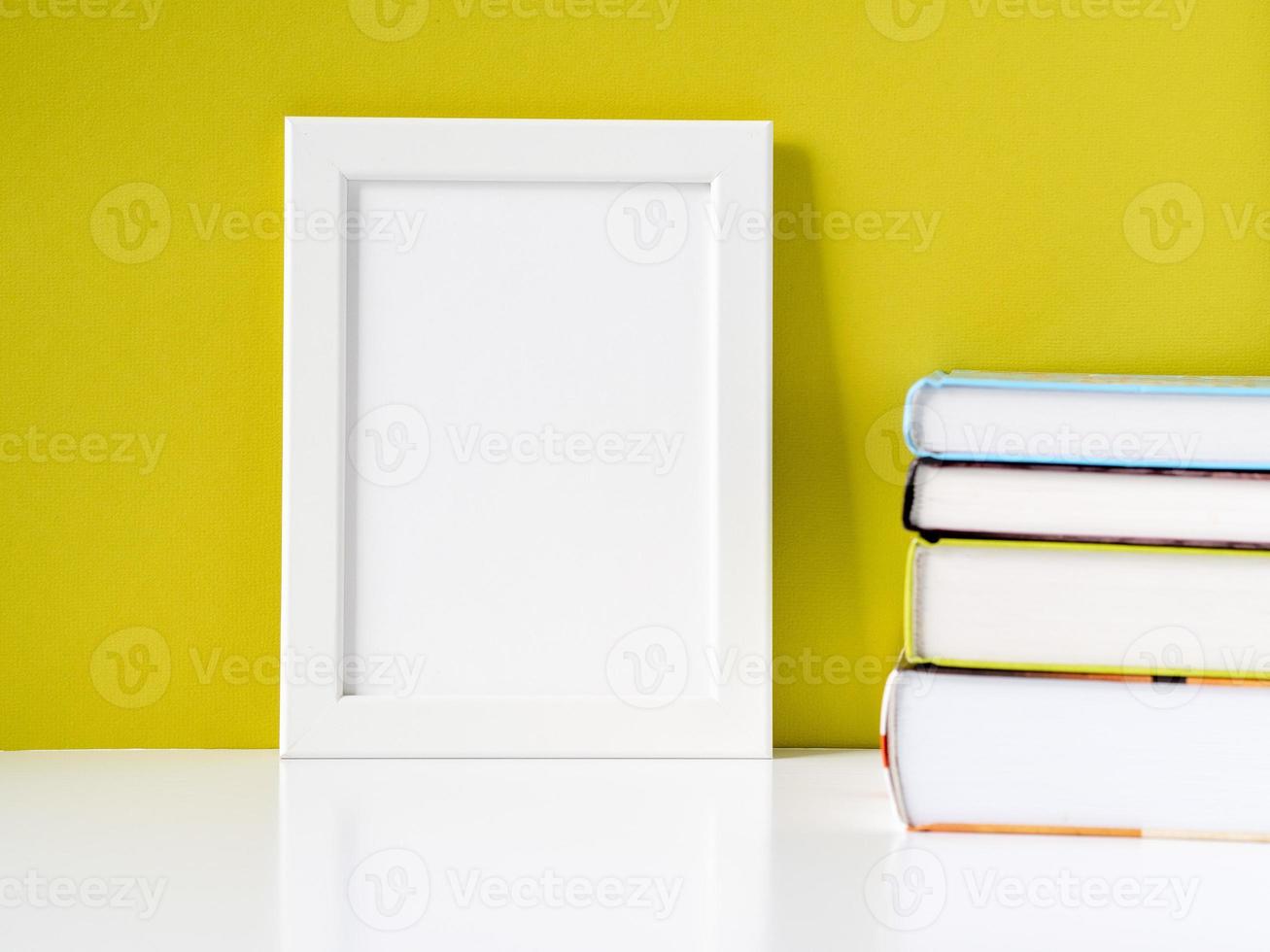 marco blanco en blanco y pila de libros sobre una mesa blanca contra la pared de color oliva con espacio para copiar foto