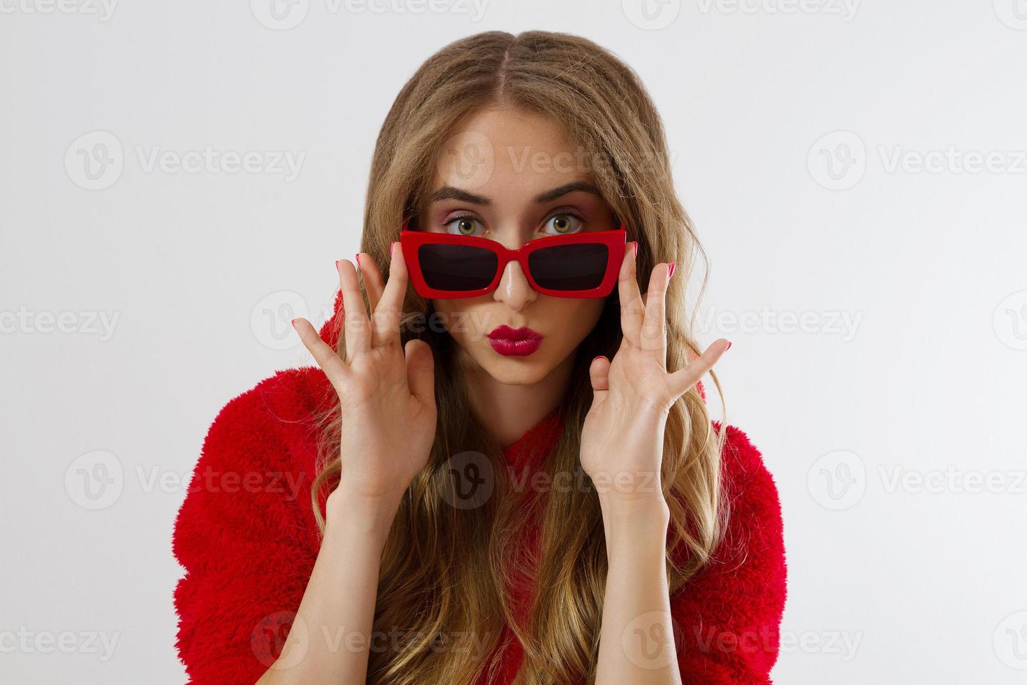 Closeup woman face with red lips, sunglasses hoodie isolated on white background. Fashionable girl in stylish outfit. Makeup, beauty concept. Winter autumn clothes. Shock excited female face. Close up photo