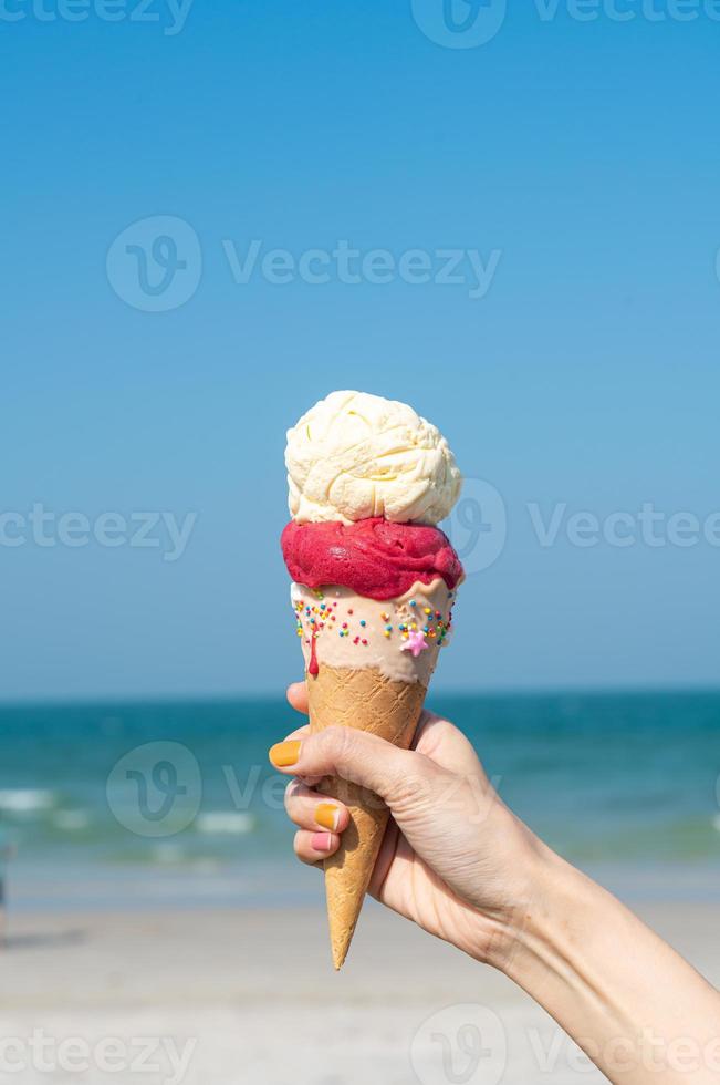 mano que sostiene el cono de helado con fondo de cielo azul foto