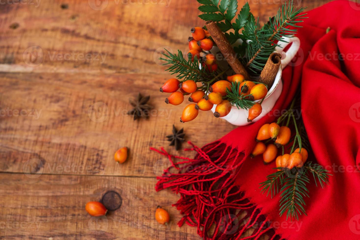 composition with a cup with thorn berries spruce branches and a red scarf on a wooden background photo