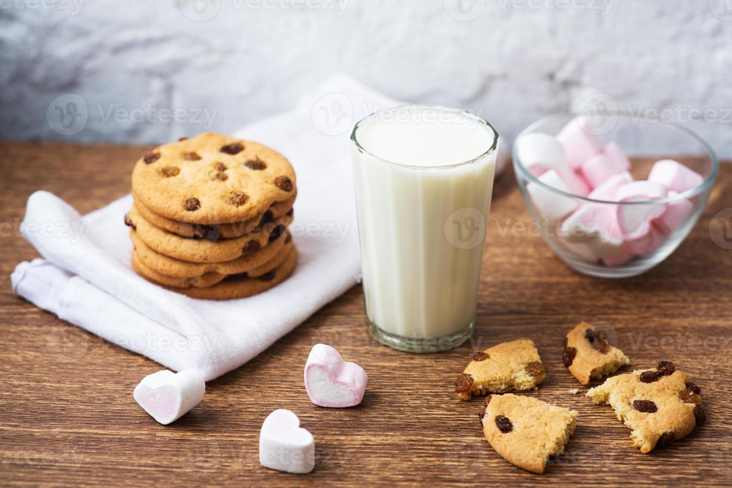 galletas caseras con leche y malvavisco de aire sobre papel de cocina y mesa de madera. buenos días. concepto de desayuno foto