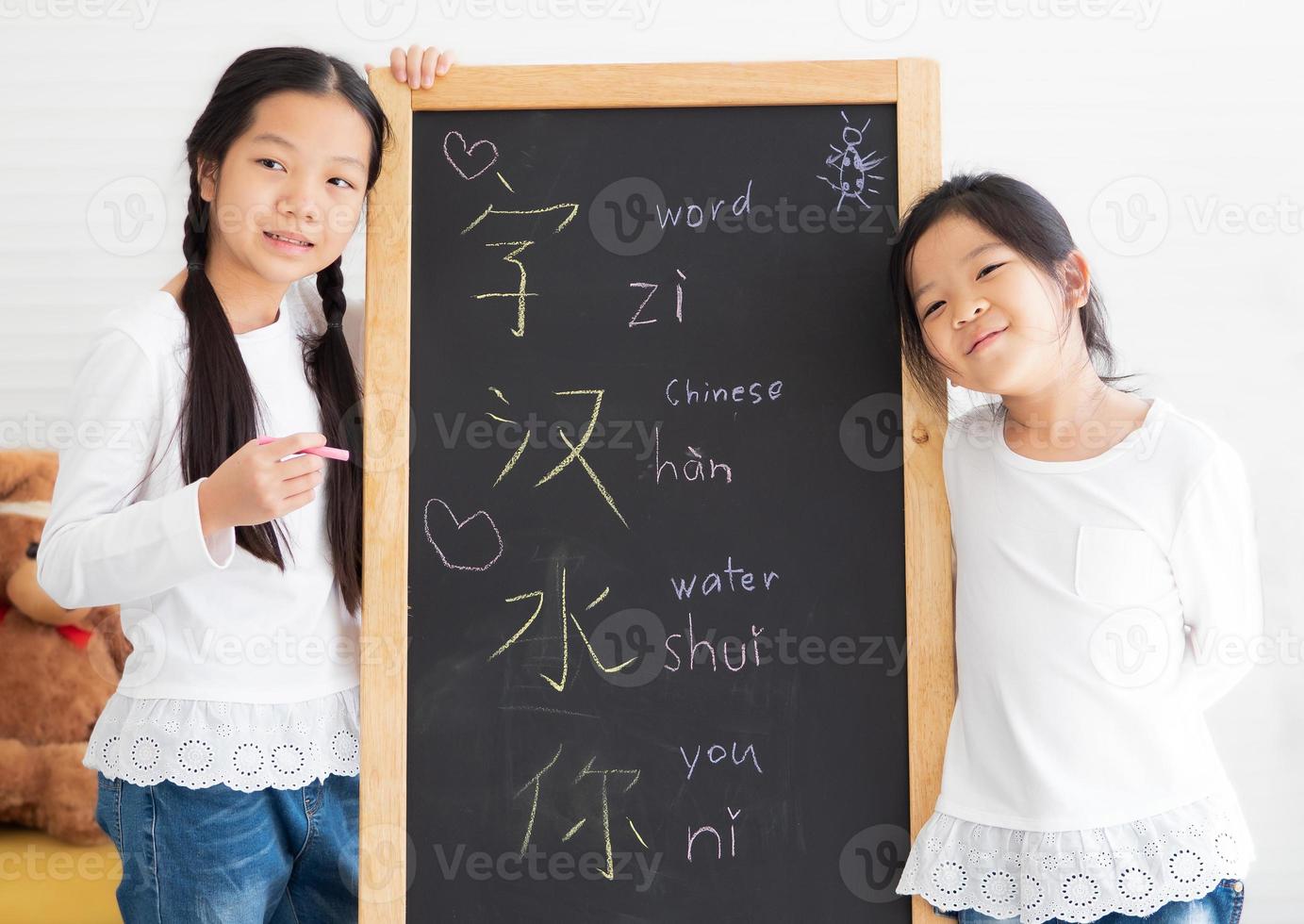 dos niños pequeños de pie junto a la pizarra feliz escribiendo texto chino. los jóvenes hermanos asiáticos estudian juntos en casa, aprenden fácilmente el idioma chino, escriben en la pizarra. estilo de vida de los niños que educan en el hogar. foto
