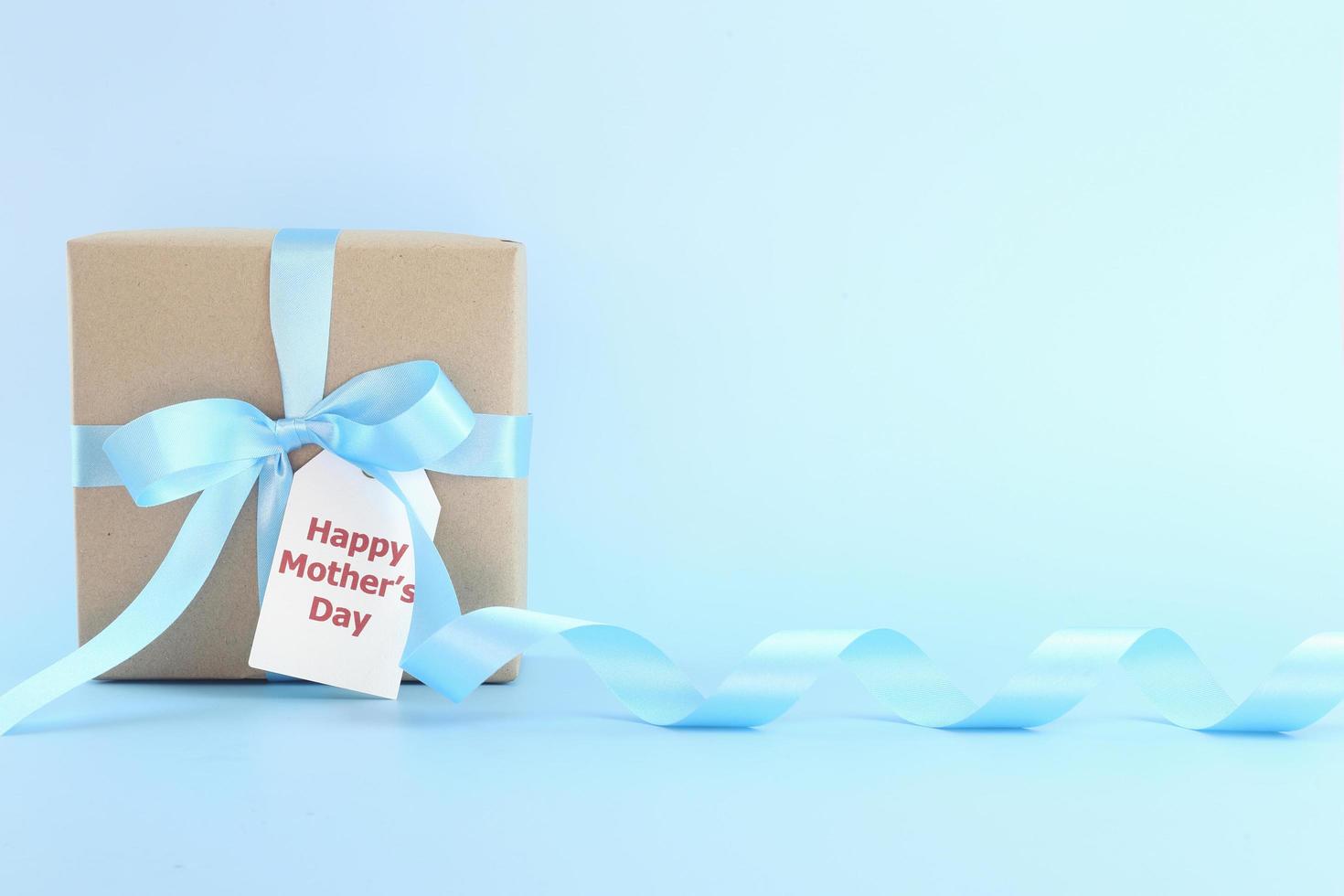 Mother's day background. Closed up brown gift box with blue bows - long ribbon and card on pastel blue background with copy space. I love mom concept. photo