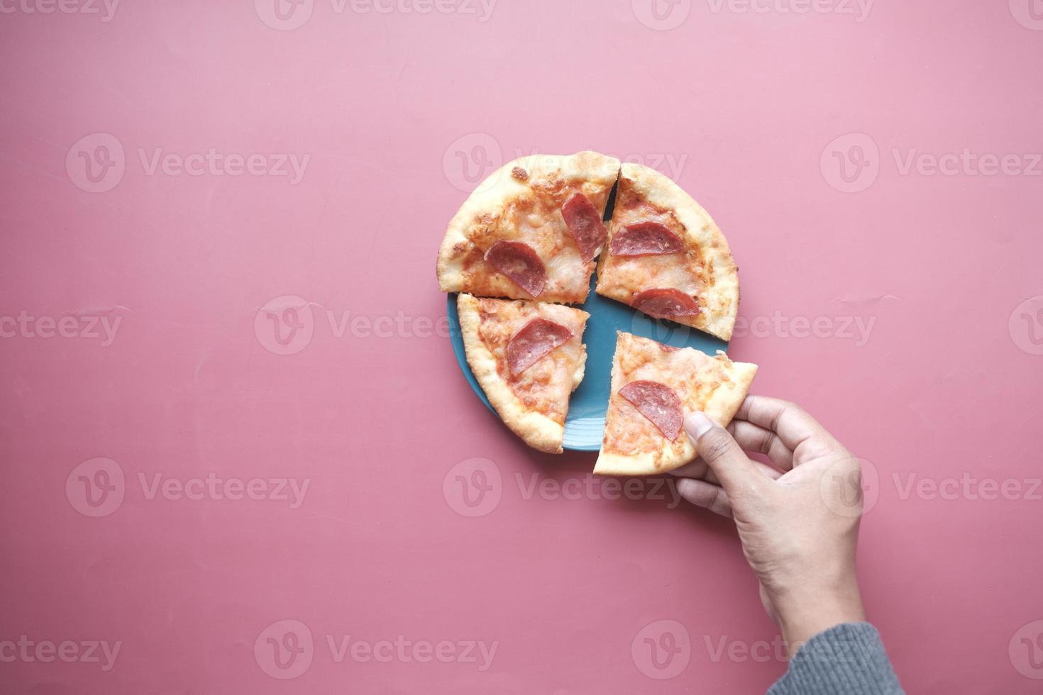 top view of man hand picking slice of pizza from a plate photo