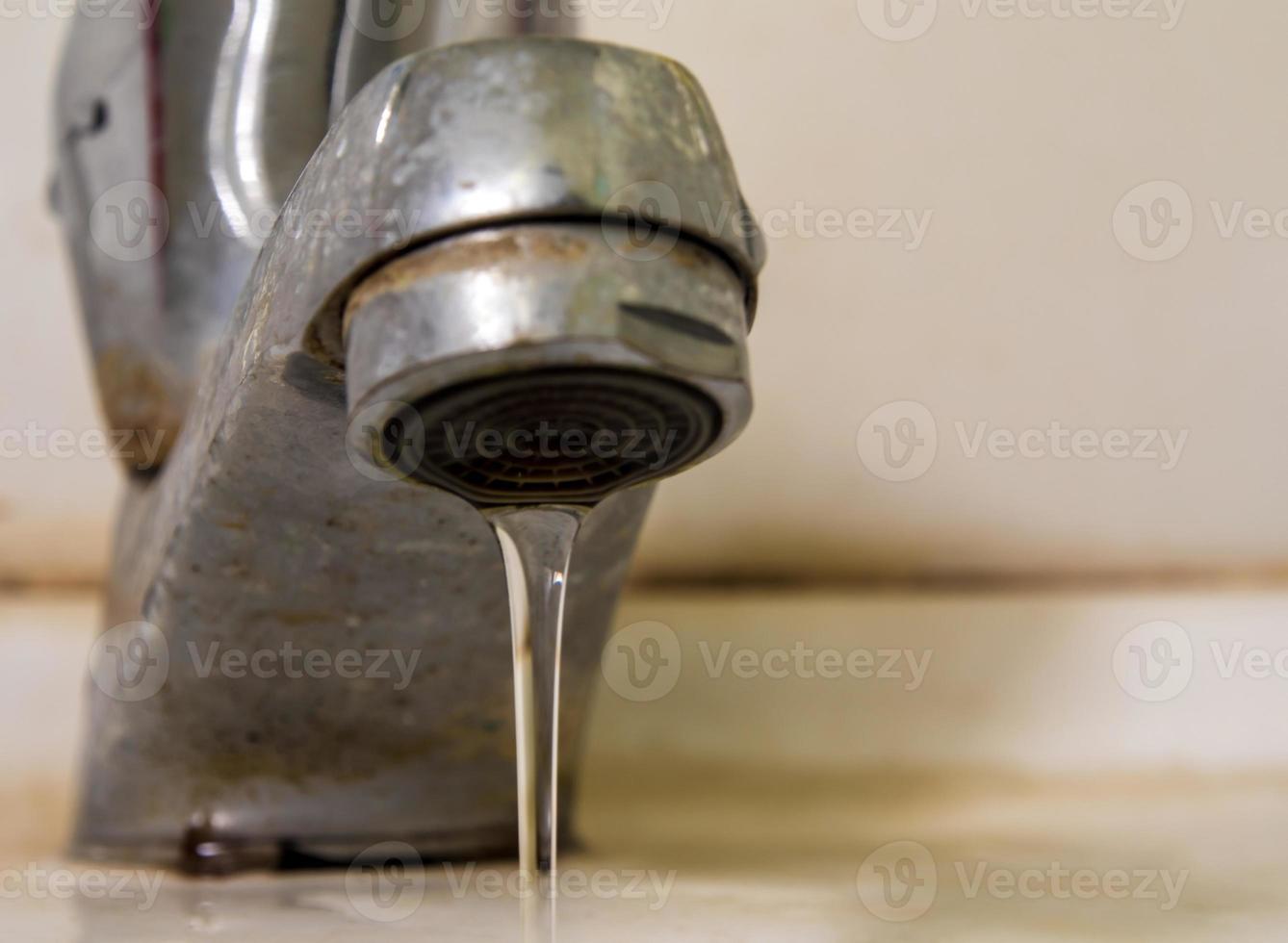 Leaking water drops from old rust and stained faucet photo