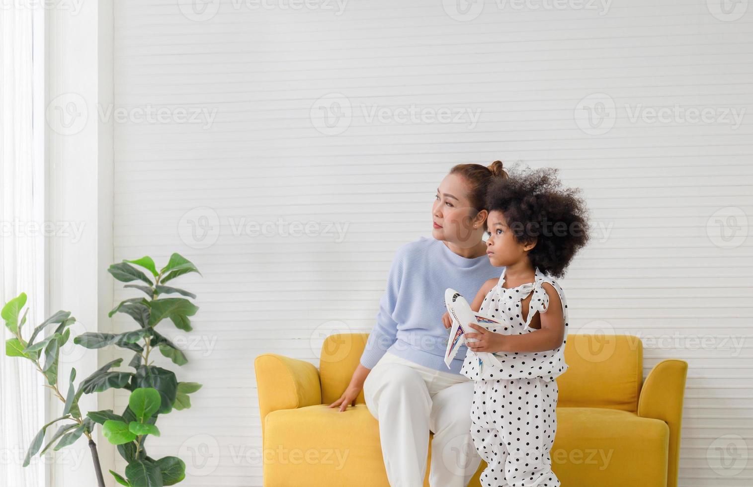 Little kid girl and grandmother playing cheerfully in living room, grandmother and child looking outside through the window photo