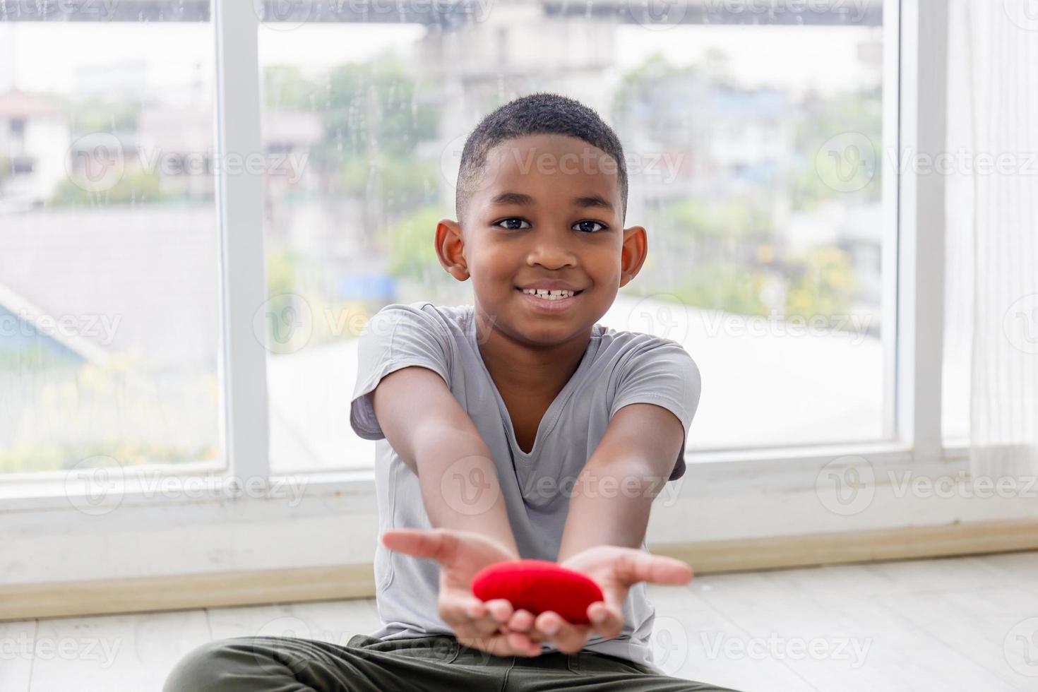 niño sonriente sosteniendo en forma de corazón rojo en la sala de estar foto