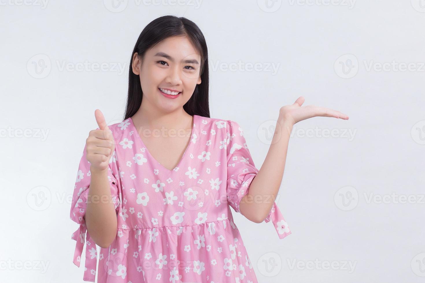 Asian beautiful woman with black long hair in white shirt shows thumb up and present something on white background. photo