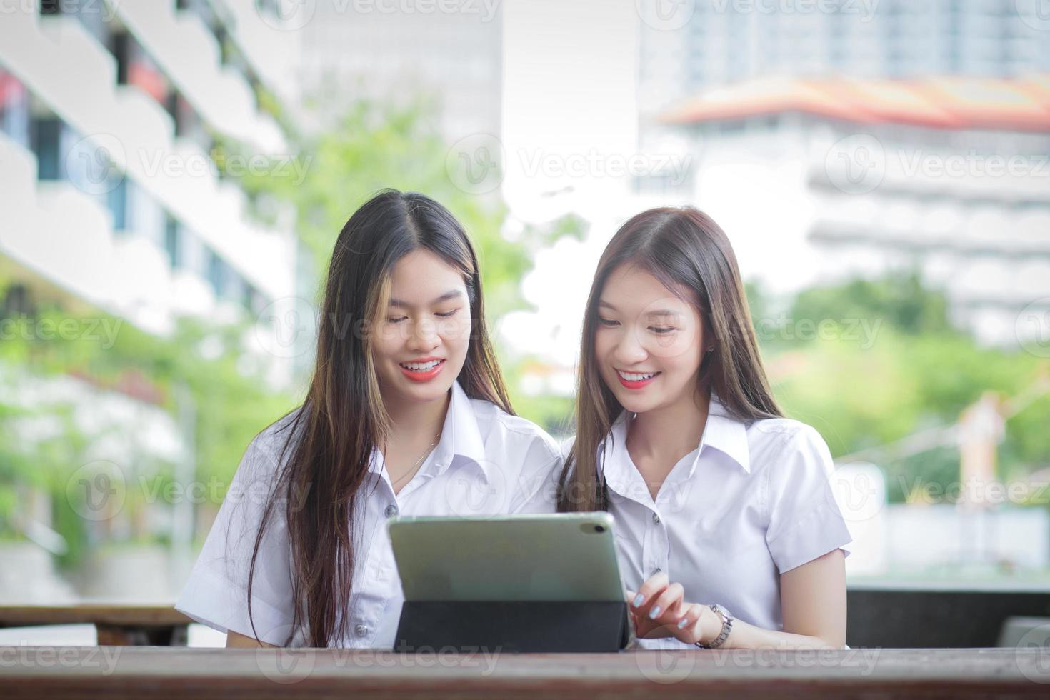Two young Asian girls students are consulting together and using a tablet to search information for a study report. photo