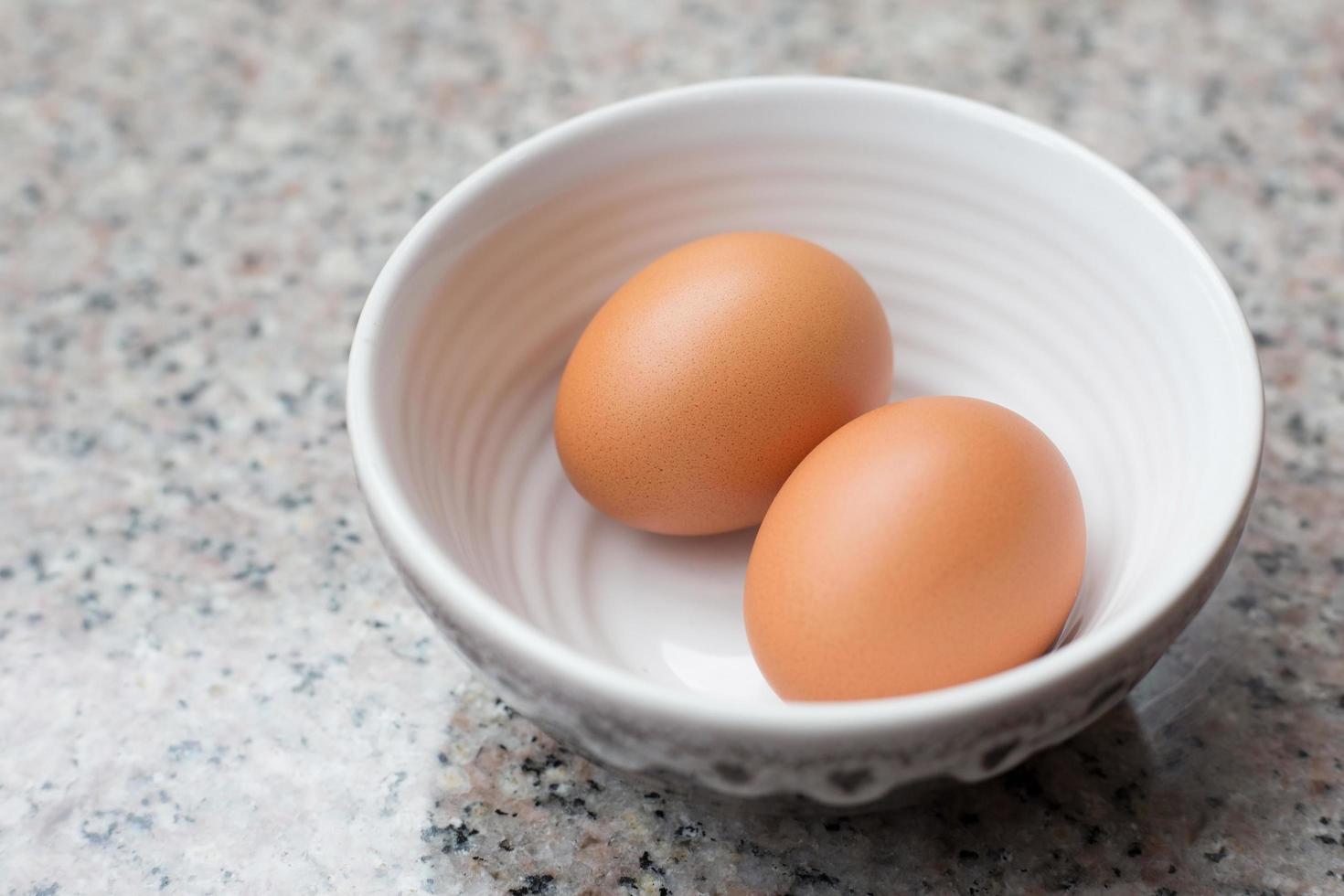 dos huevos frescos de color marrón claro en una taza sobre una mesa de granito. foto