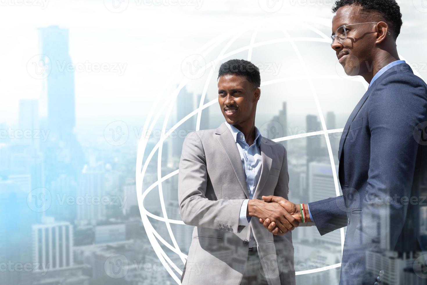 young modern men in smart casual wear shaking hands. Two smiling businessmen shaking hands together. Two confident businessmen shaking hands and looking for the future. World logo behind the men. photo