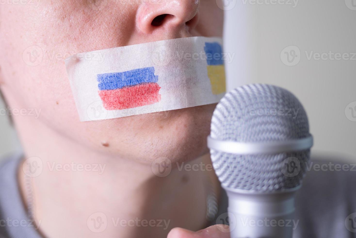 una boca con cinta adhesiva con una bandera de rusia y ucrania tratando de hablar por un micrófono. foto