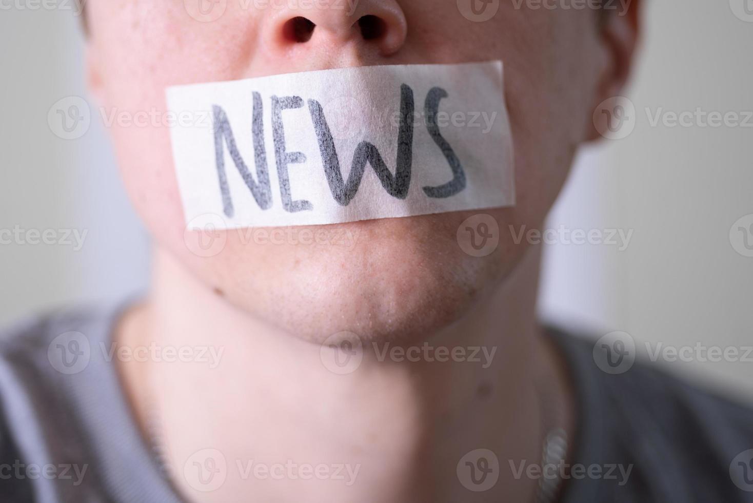 A man gags his mouth with duct tape that reads the news. photo