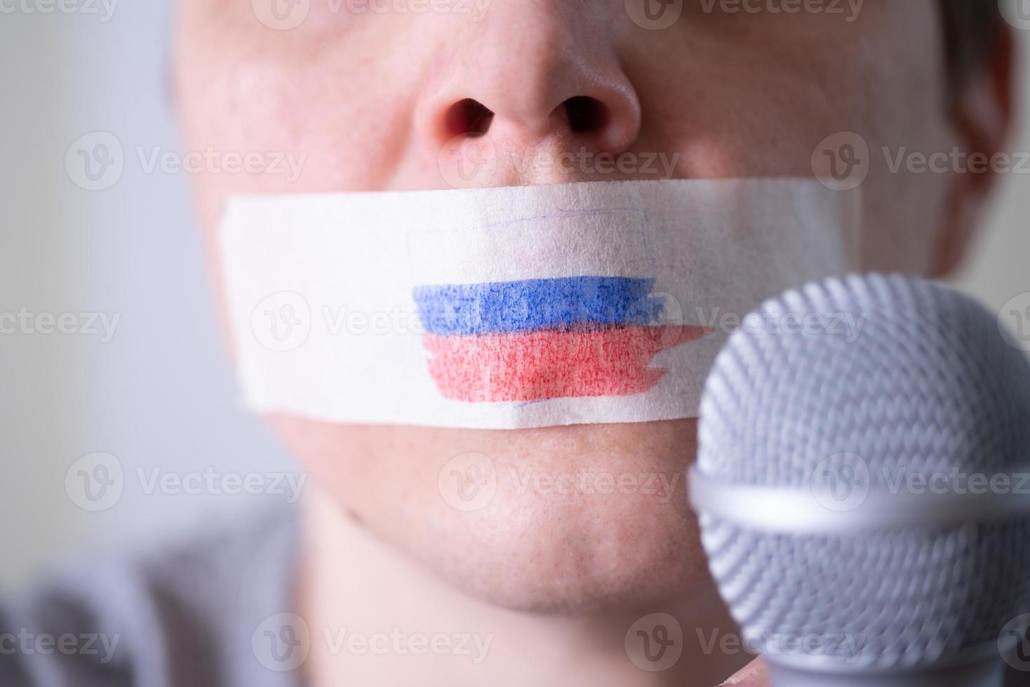 una boca tapada con cinta adhesiva con una bandera rusa, tratando de hablar por un micrófono. foto