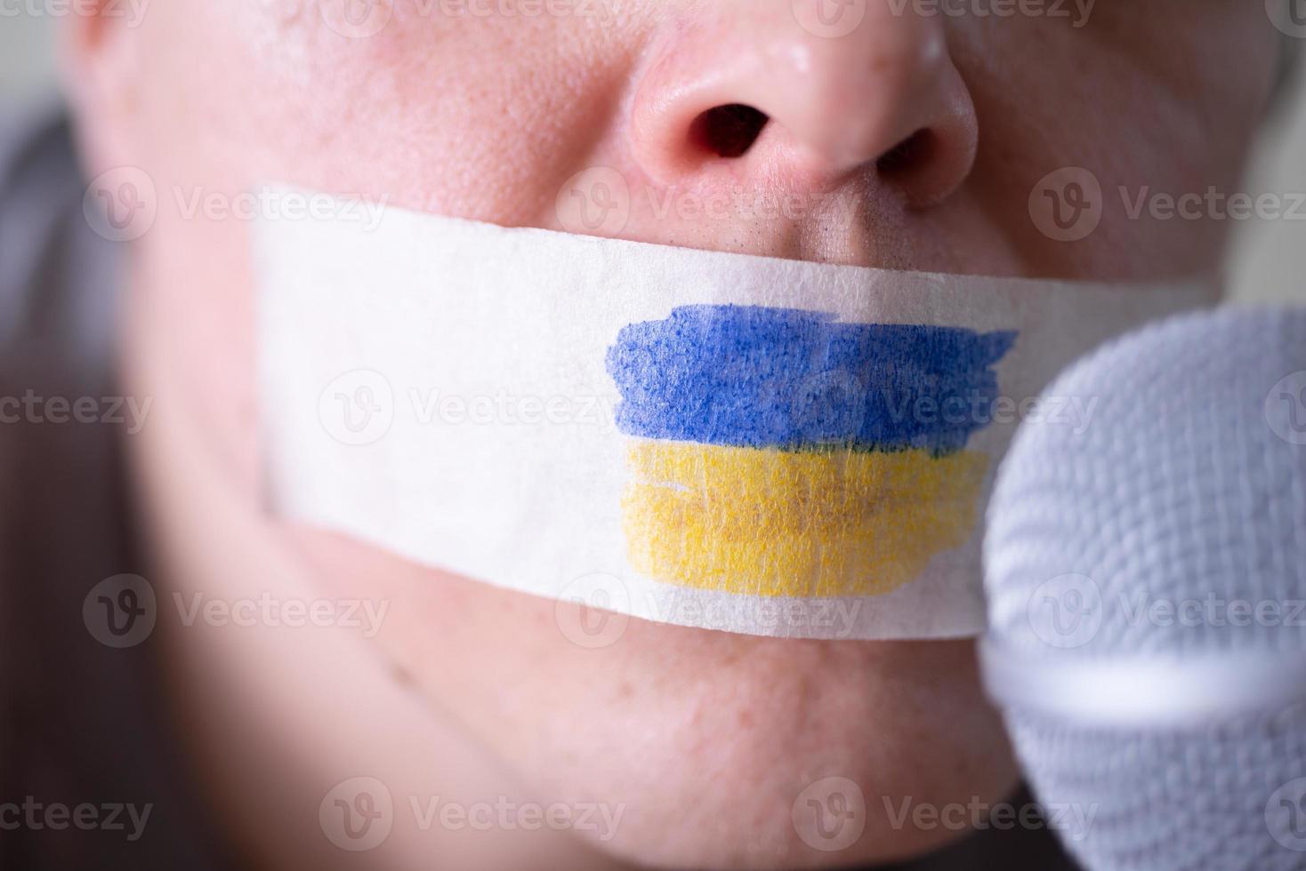 Tape over his mouth with the flag of Ukraine, trying to speak into a microphone. photo