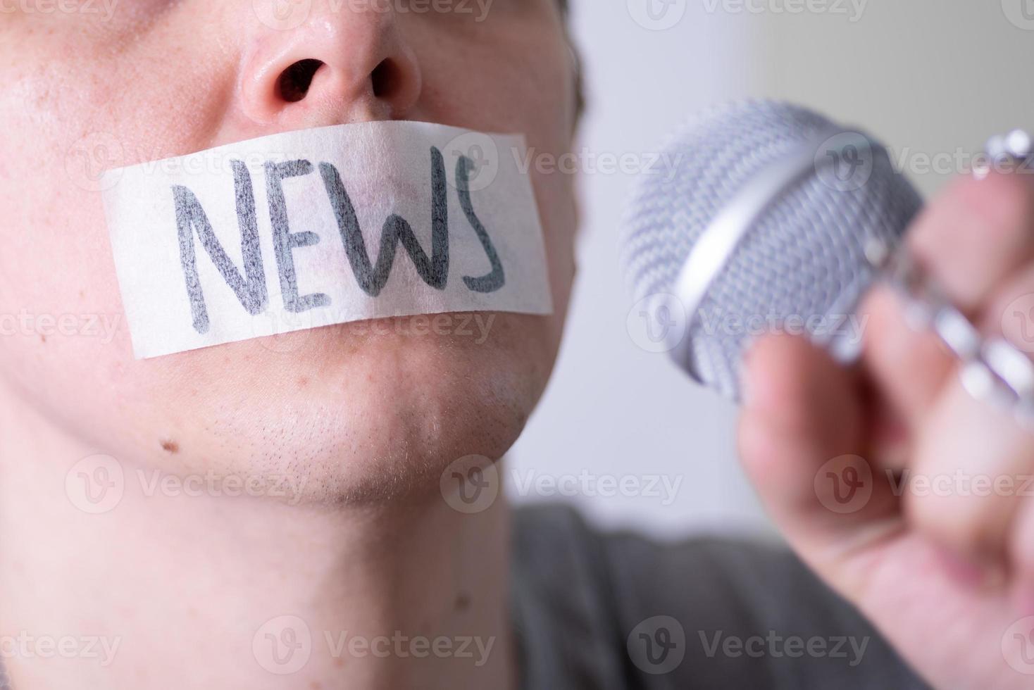 A man gags his mouth with duct tape saying news trying to speak into a microphone. photo