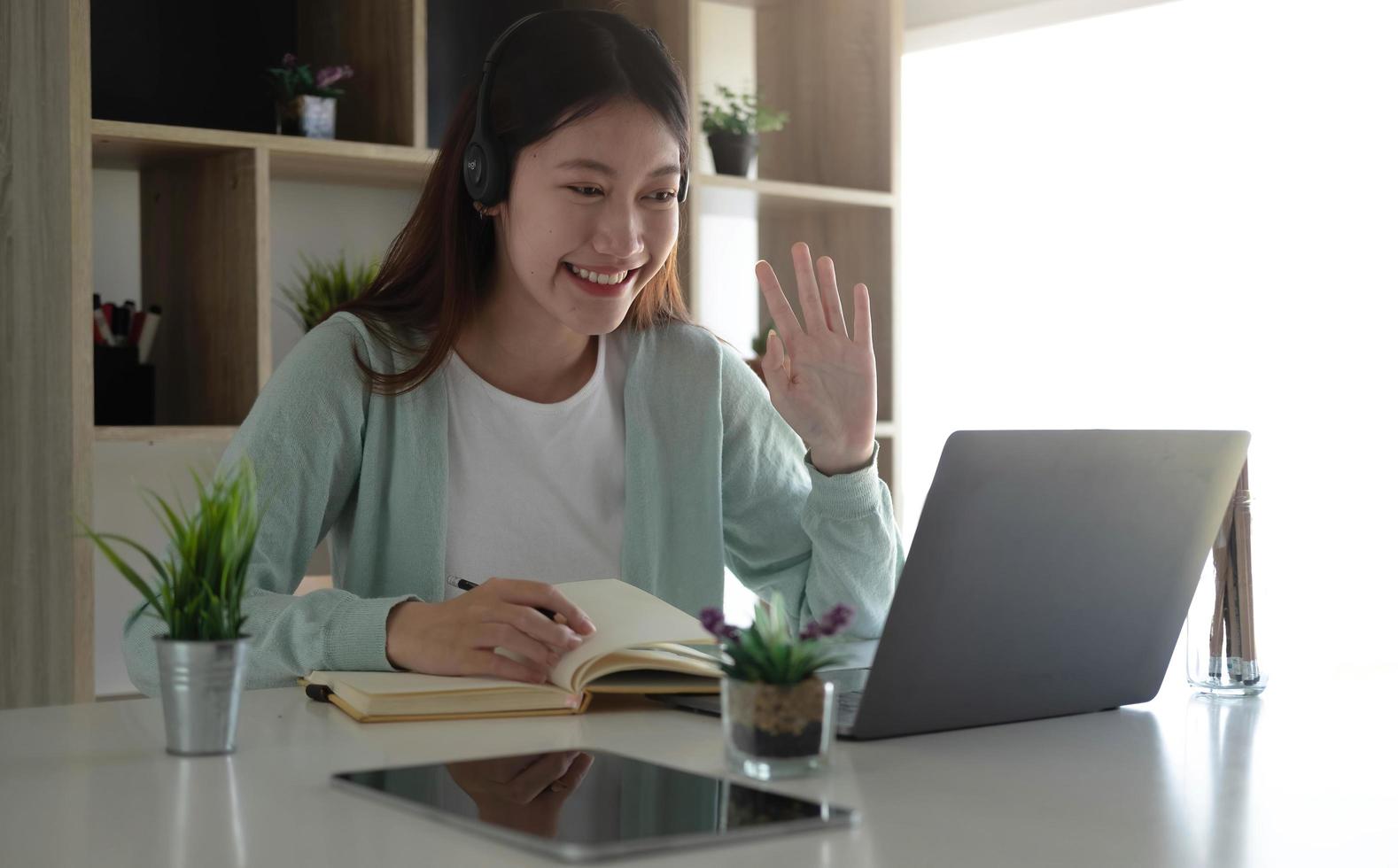 An Asian student in casual clothes is greeting her friend at a video conference. During the time of studying online at home photo