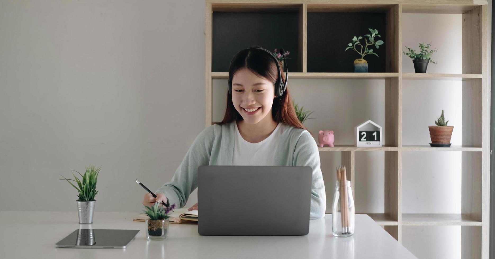 Asian schoolgirl in casual clothes is reading and doing homework video conference e-learning with teacher on laptop computer at home photo