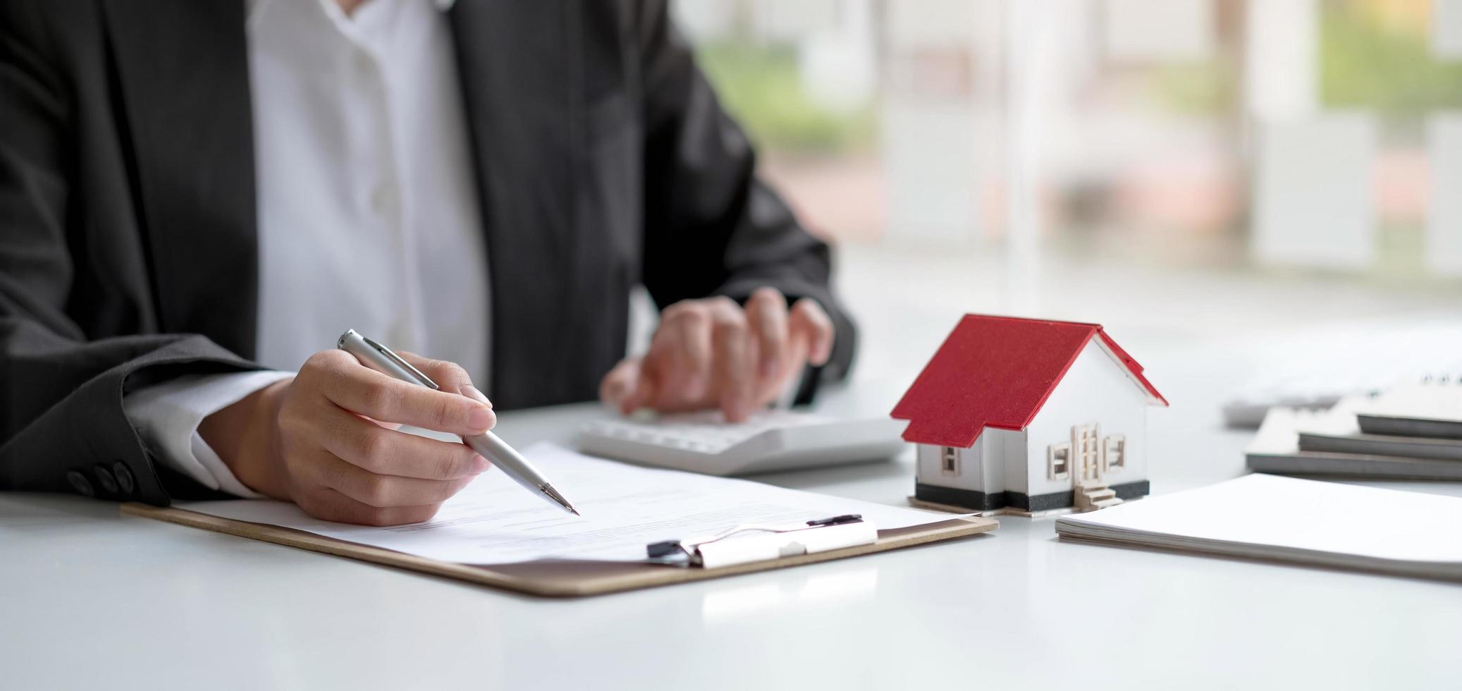 hombre de negocios o funcionario bancario que trabaja en la mesa de la oficina usando una calculadora para calcular el presupuesto financiero, el documento del préstamo, el precio de la casa. agente inmobiliario y concepto de préstamo hipotecario. foto