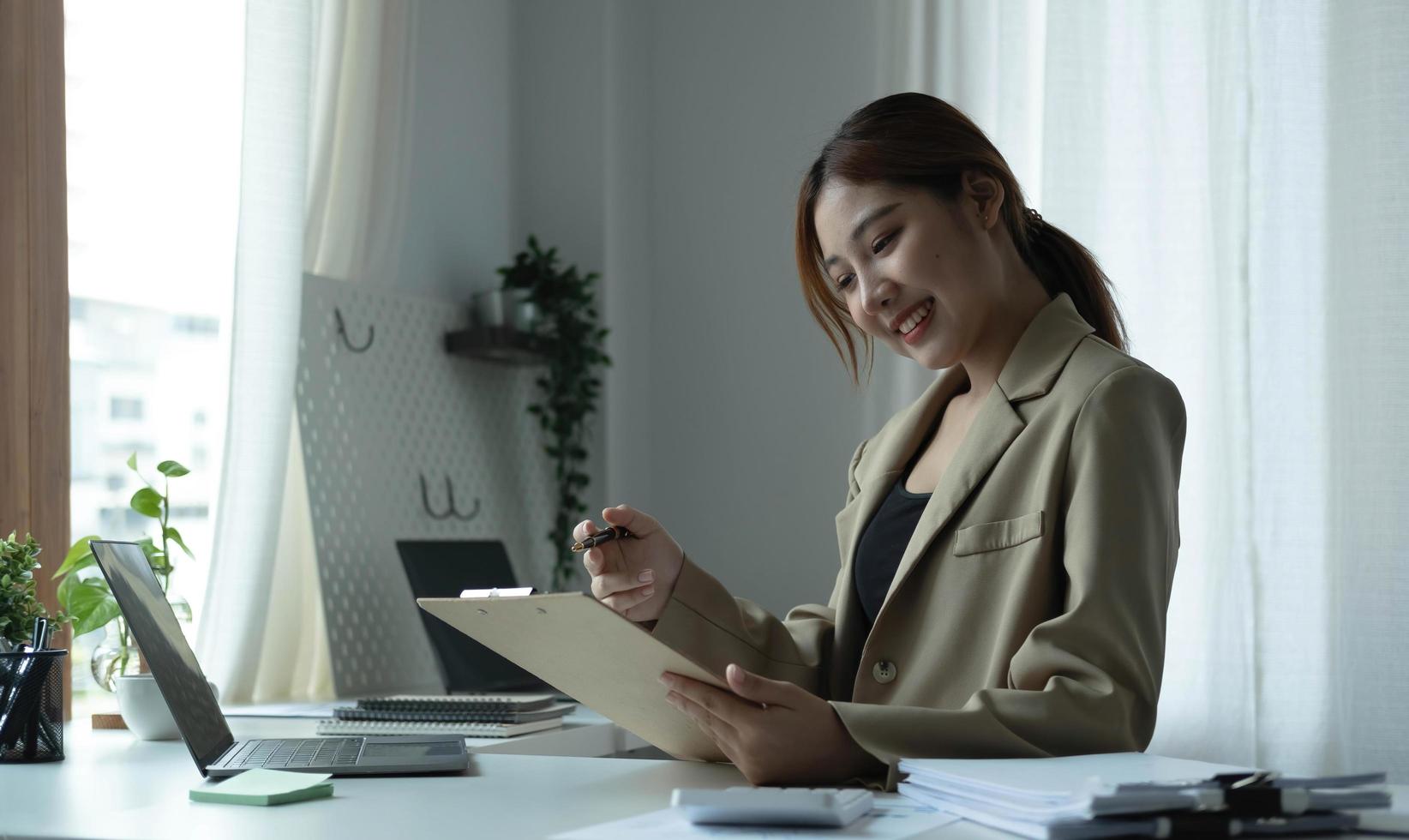 Attractive young woman sitting and her workplace and checking information on clipboard. photo