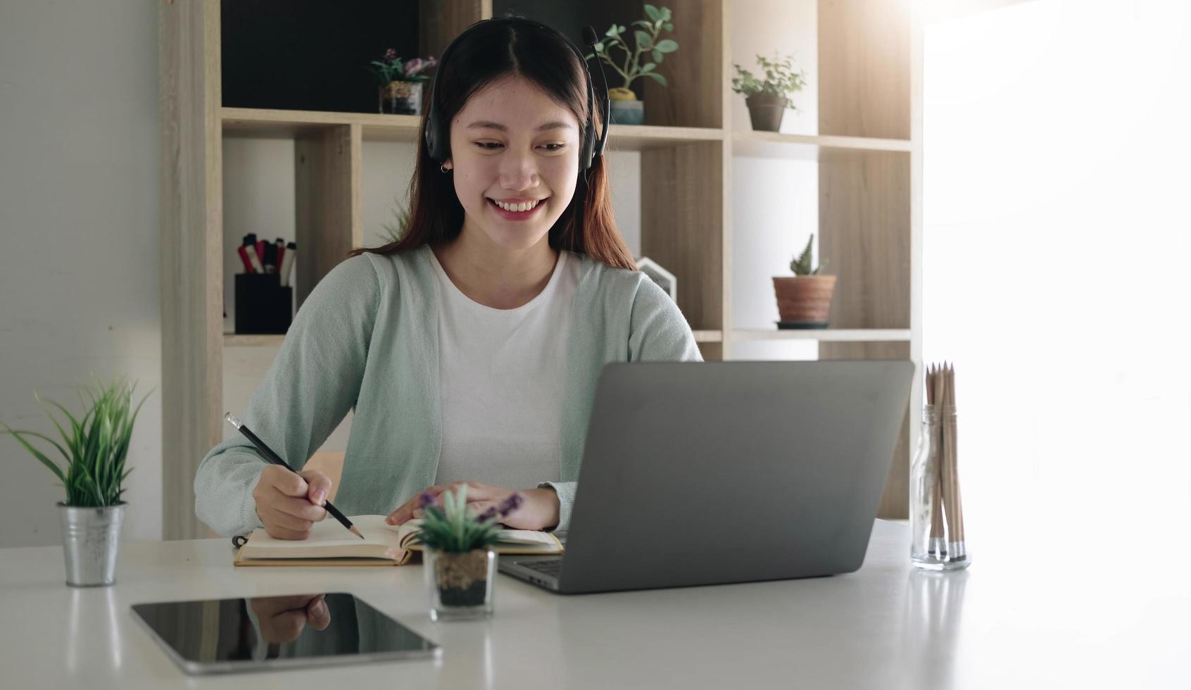 Asian schoolgirl in casual clothes is reading and doing homework video conference e-learning with teacher on laptop computer at home photo