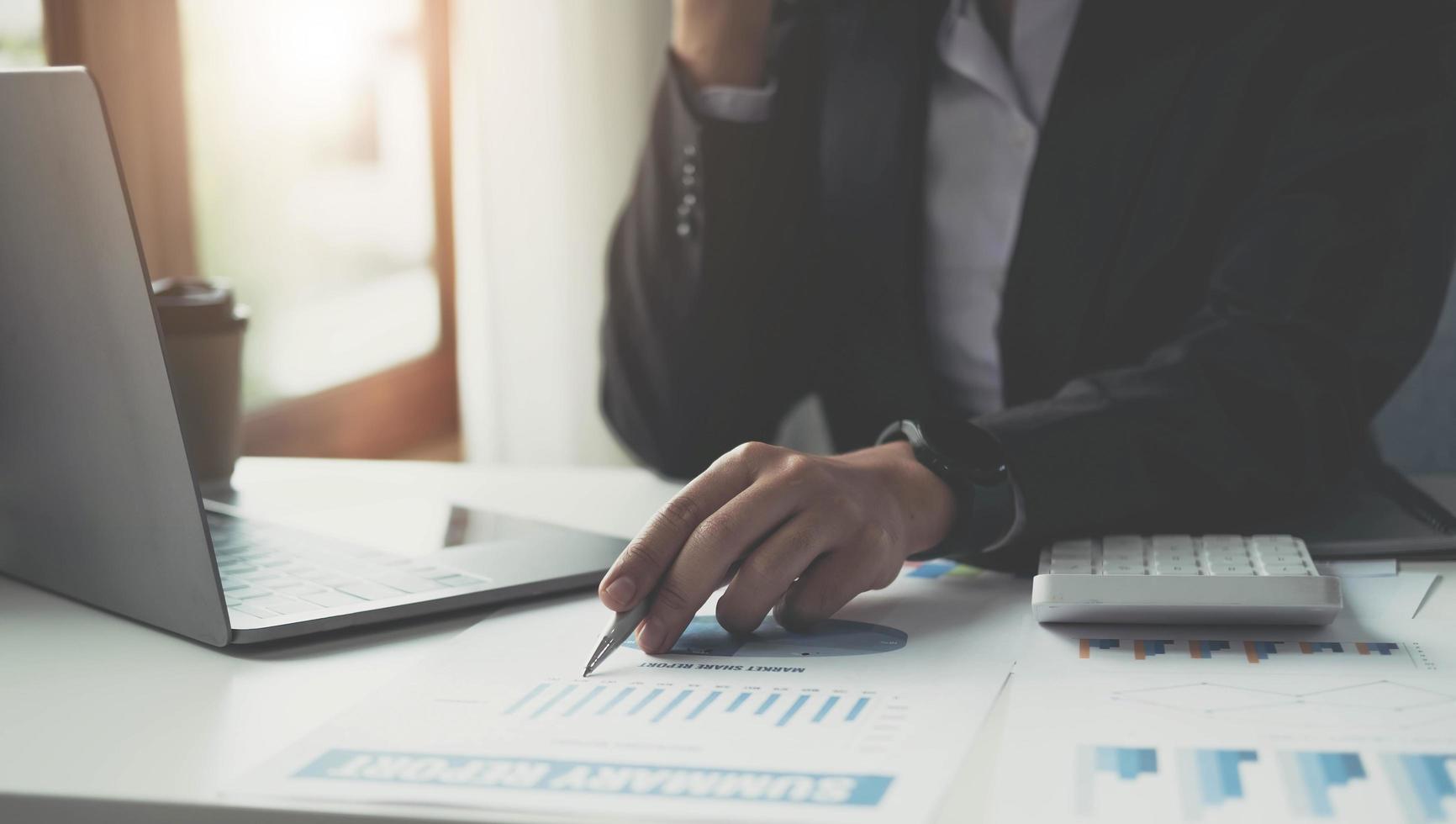 Close up Businesswoman consultant holding pen and pointing at financial on wooden desk in coffee shop. freelance, tax, accounting, statistics and analytic research concept. photo