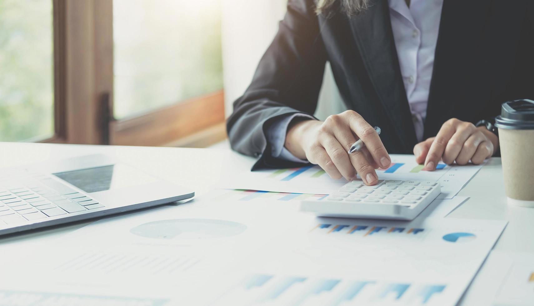 Close up Business woman using calculator and laptop for do math finance on wooden desk in office and business working background, tax, accounting, statistics and analytic research concept photo