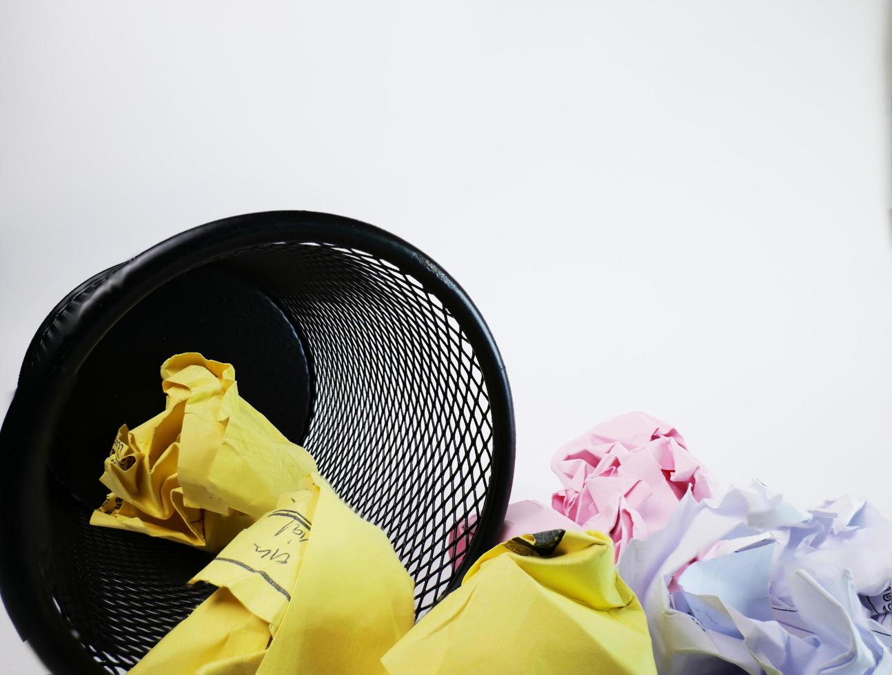 A small black basket made of round iron fell down. It is used to put the trash, documents that are not working and are overflowing to the outside. In the white background there is a copy space. photo