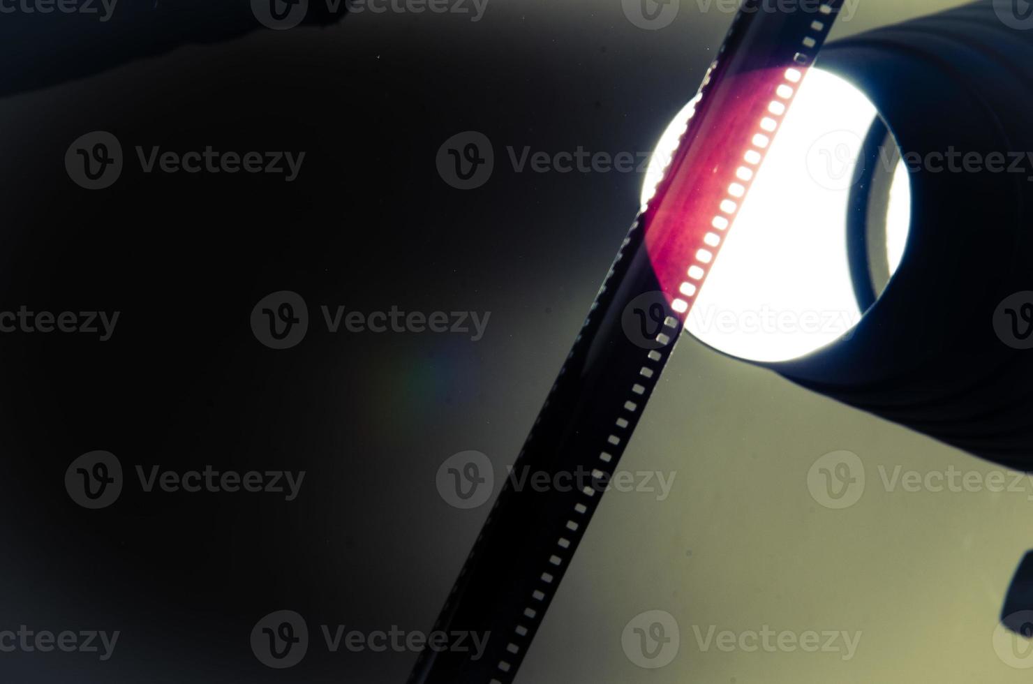 An old roll of negative held against the light shows the red yellow texture of old films and black and white cinema. photo