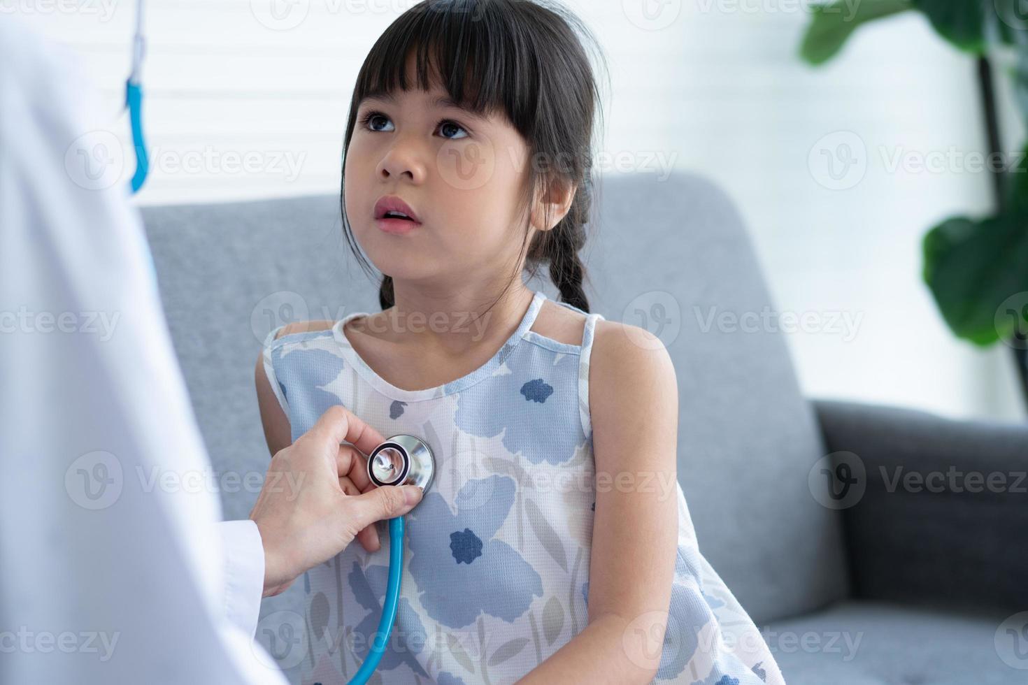 una médica pediatra asiática sostiene un estetoscopio para examinar a una niña paciente y al diablo los pulmones de un niño, un buen médico de familia que visita a un niño en casa, atención médica y medicina para el concepto de infancia. foto