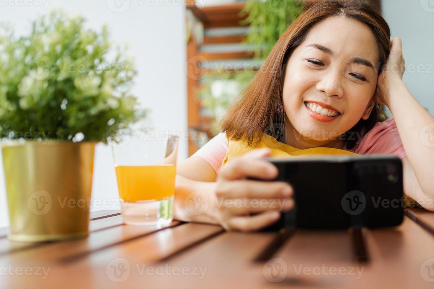 Happy Asian woman sitting in the backyard and holding smartphone for watching a movie series during relax time. photo