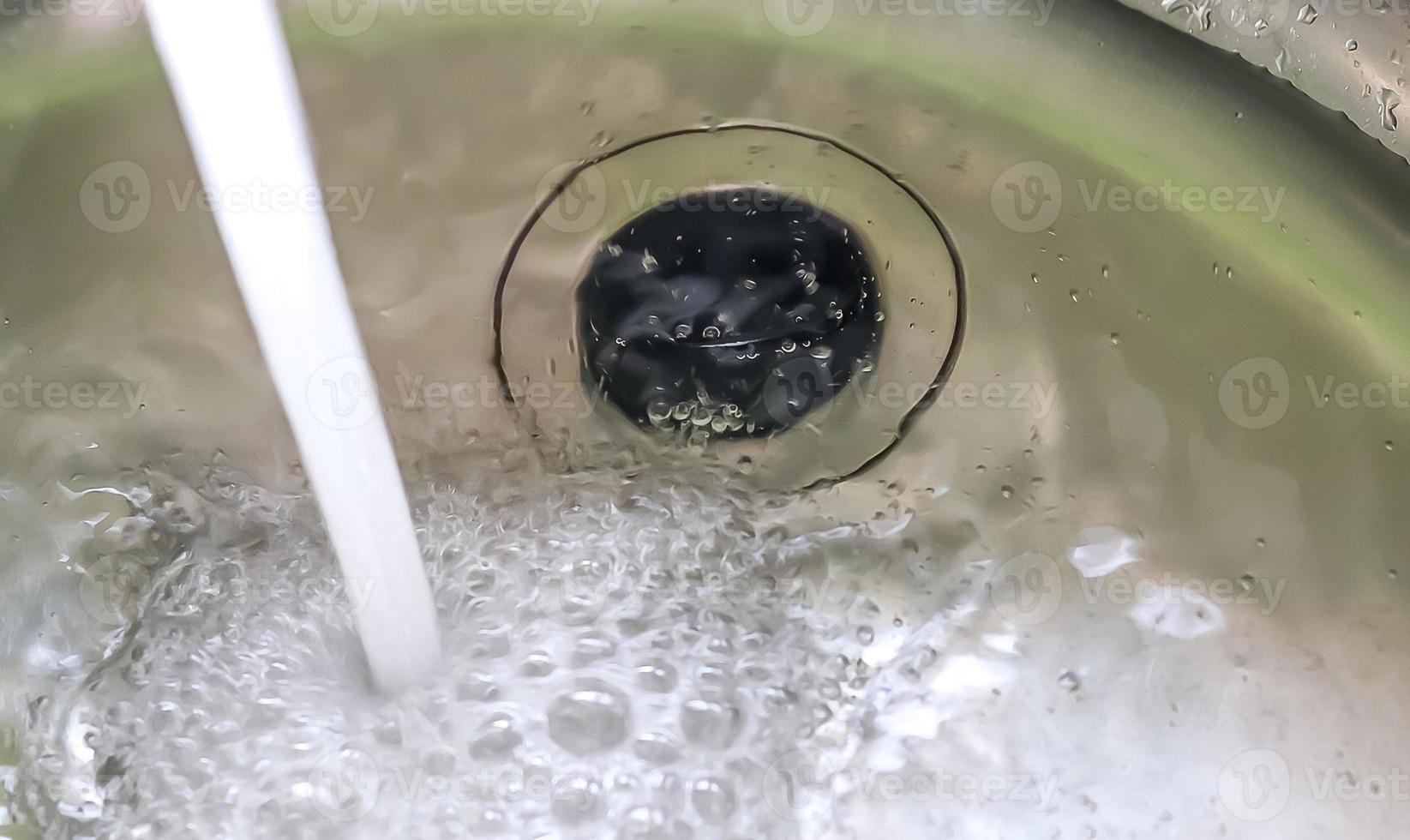 Running water from a water tap into the drain of a chrome sink. photo