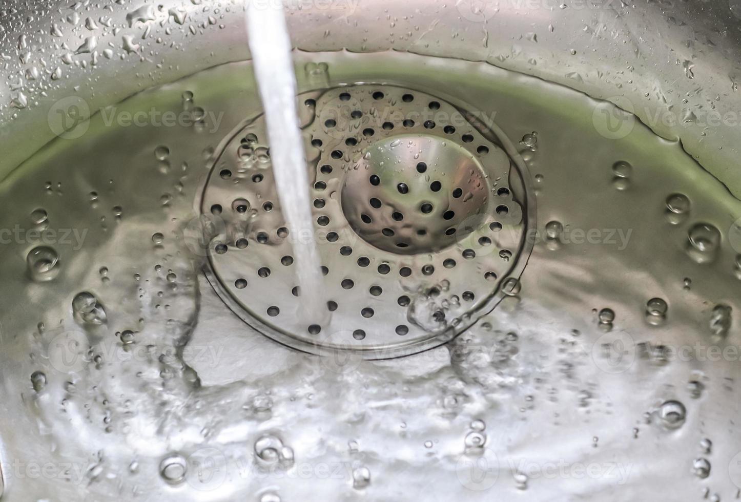 Running water from a water tap into the drain of a chrome sink. photo