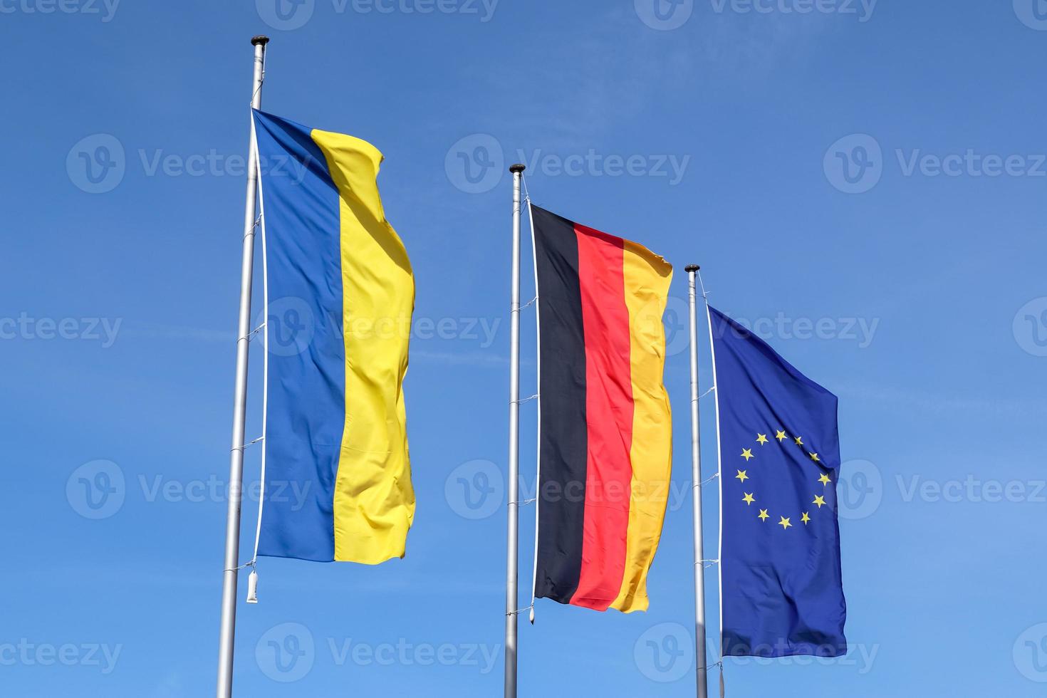 Flags of Ukraine, Germany and European Union fly side by side against blue sky. photo