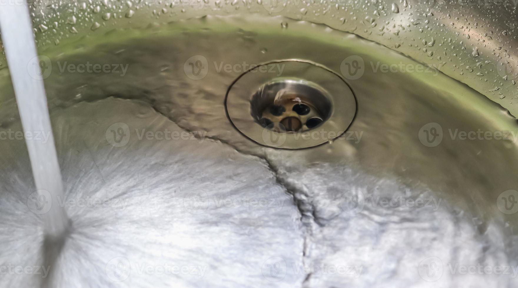 agua corriente de un grifo de agua en el desagüe de un fregadero de cromo. foto