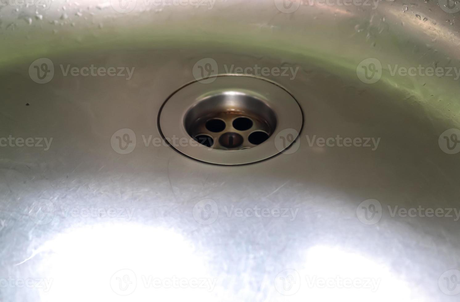 Running water from a water tap into the drain of a chrome sink. photo