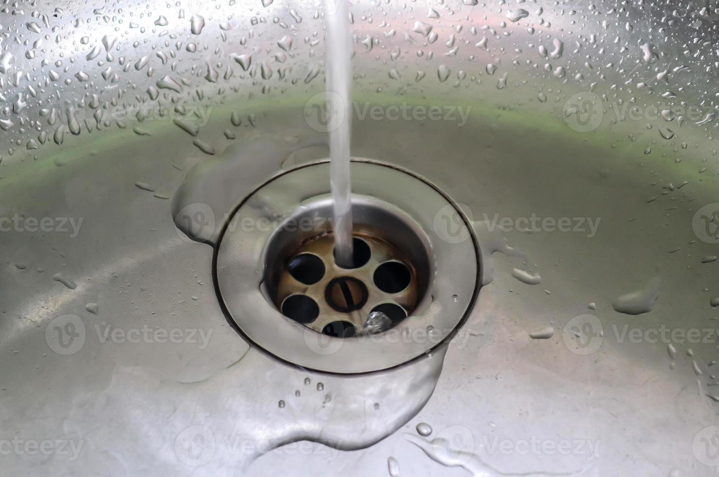 agua corriente de un grifo de agua en el desagüe de un fregadero de cromo. foto