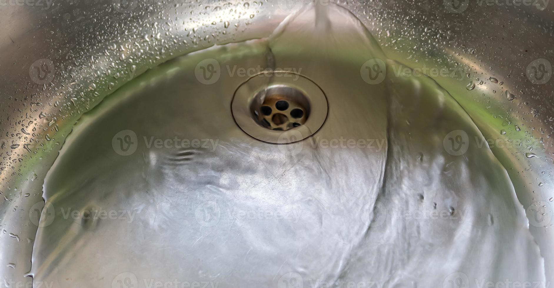 Running water from a water tap into the drain of a chrome sink. photo