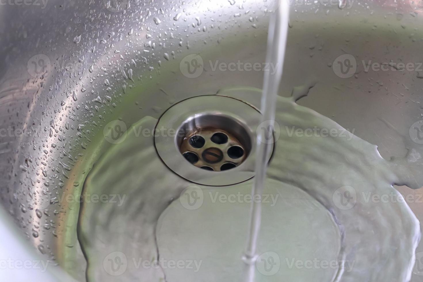 agua corriente de un grifo de agua en el desagüe de un fregadero de cromo. foto