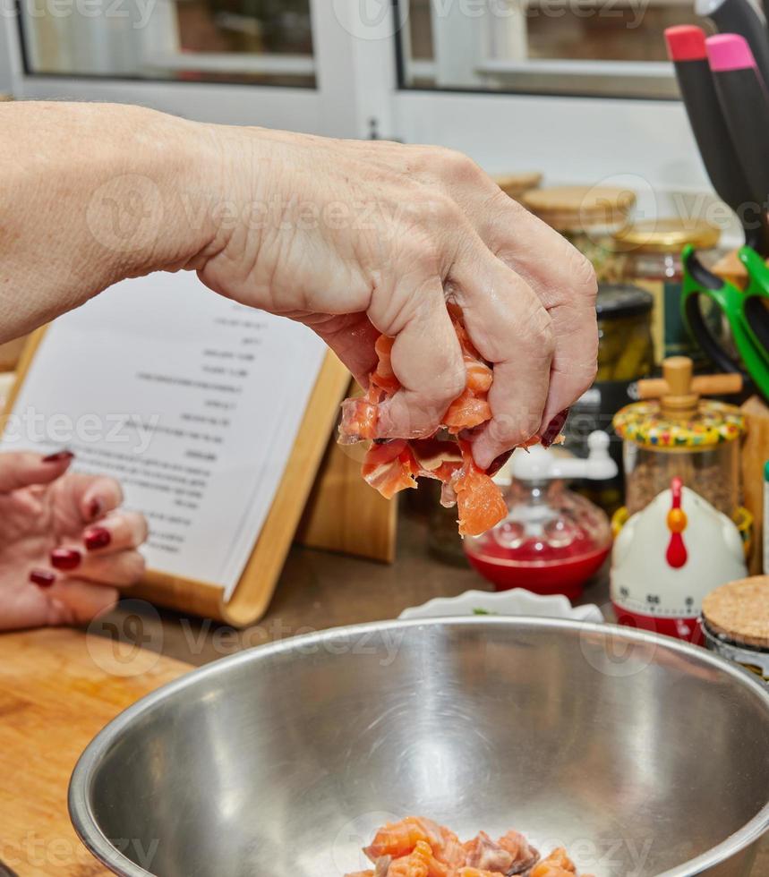 el chef arroja cubos de salmón en un tazón para preparar una receta de Internet foto